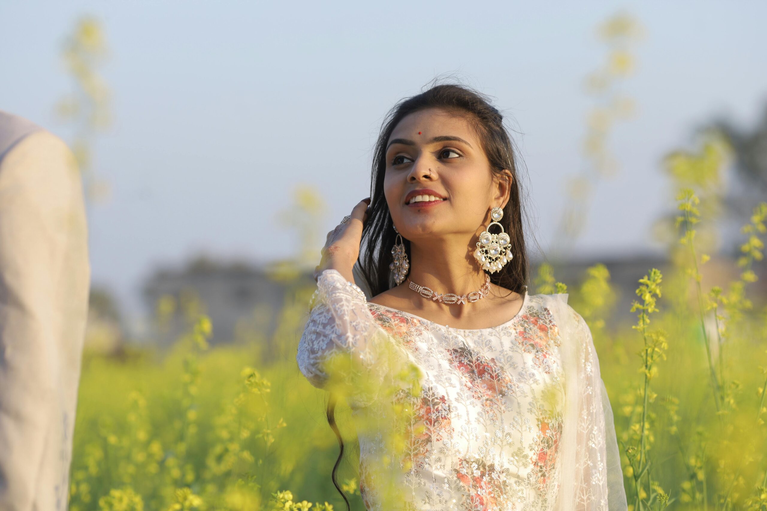 A young woman in traditional attire smiling in a vibrant mustard field.